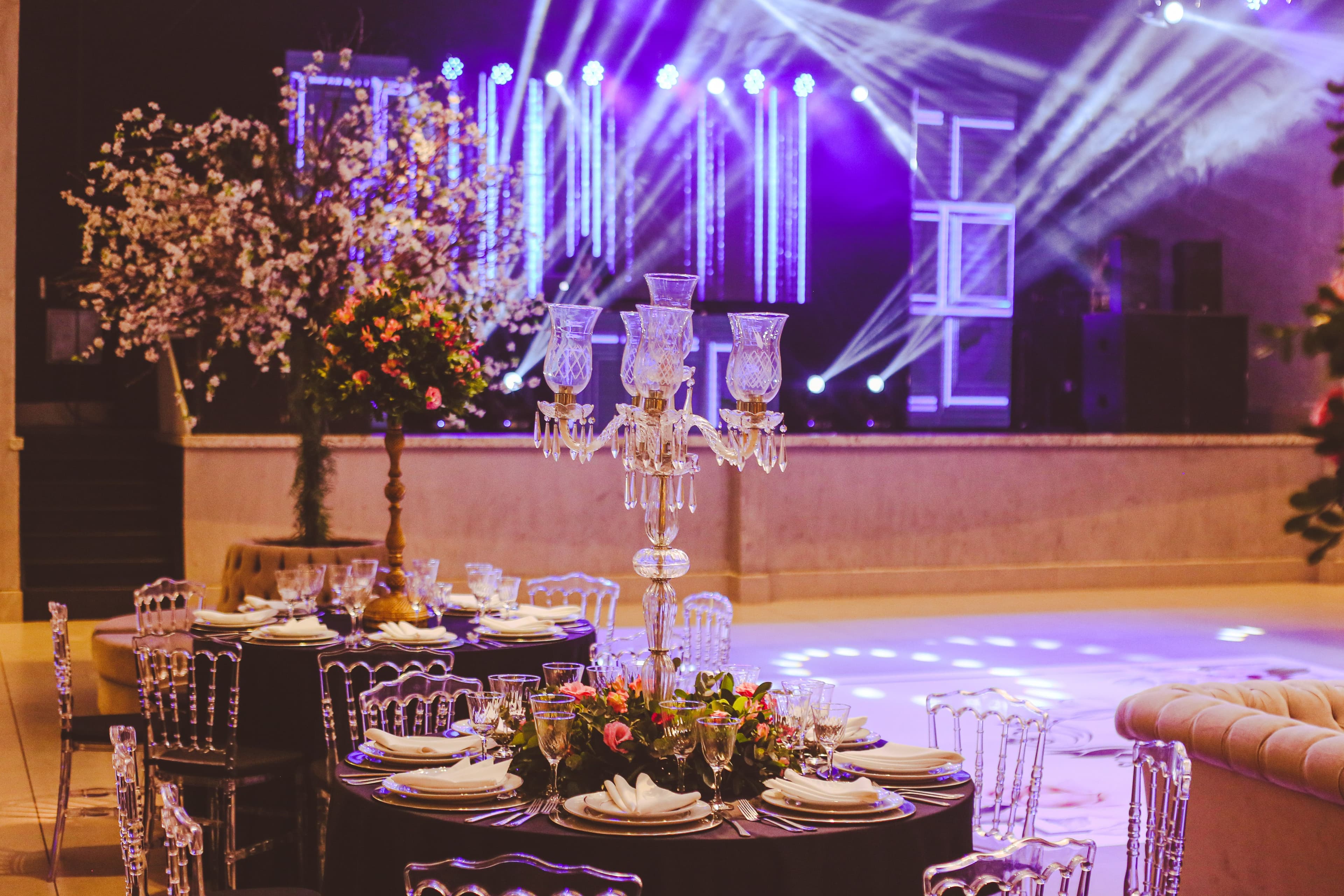 Event dining tables beside a dance floor and stage with purple and white lighting