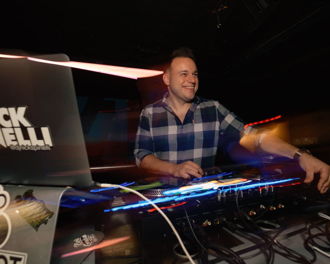 DJ smiling behind the decks with colorful light trails