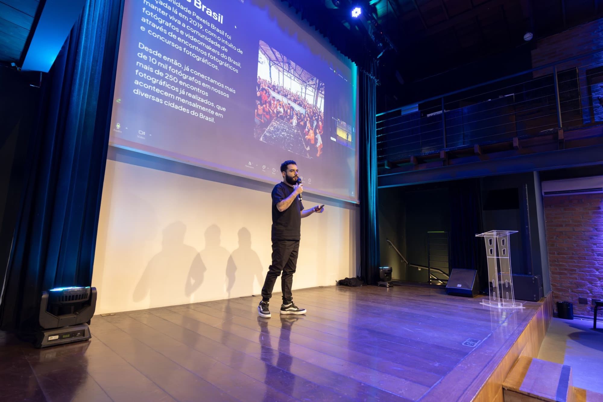 A speaker on a lit conference stage with screens behind him